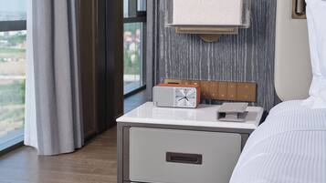 Habitación de hotel con cama, mesita de noche con reloj y cajoneras, y ventana con cortinas.