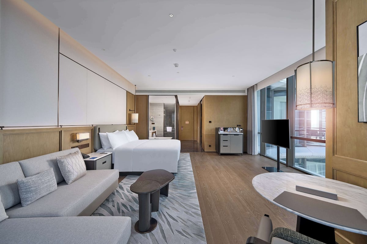 Una habitación de hotel moderna con cama, sofá, mesa de centro y escritorio con televisor.