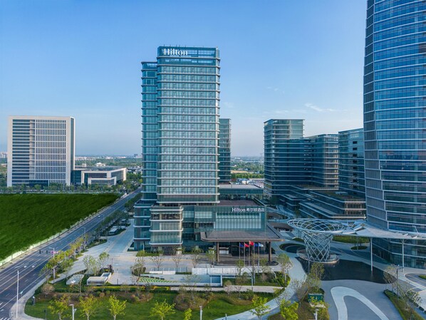 A modern Hilton hotel with a prominent glass facade, surrounded by other high-rise buildings. - Hilton Jiashan (Jiaxing)