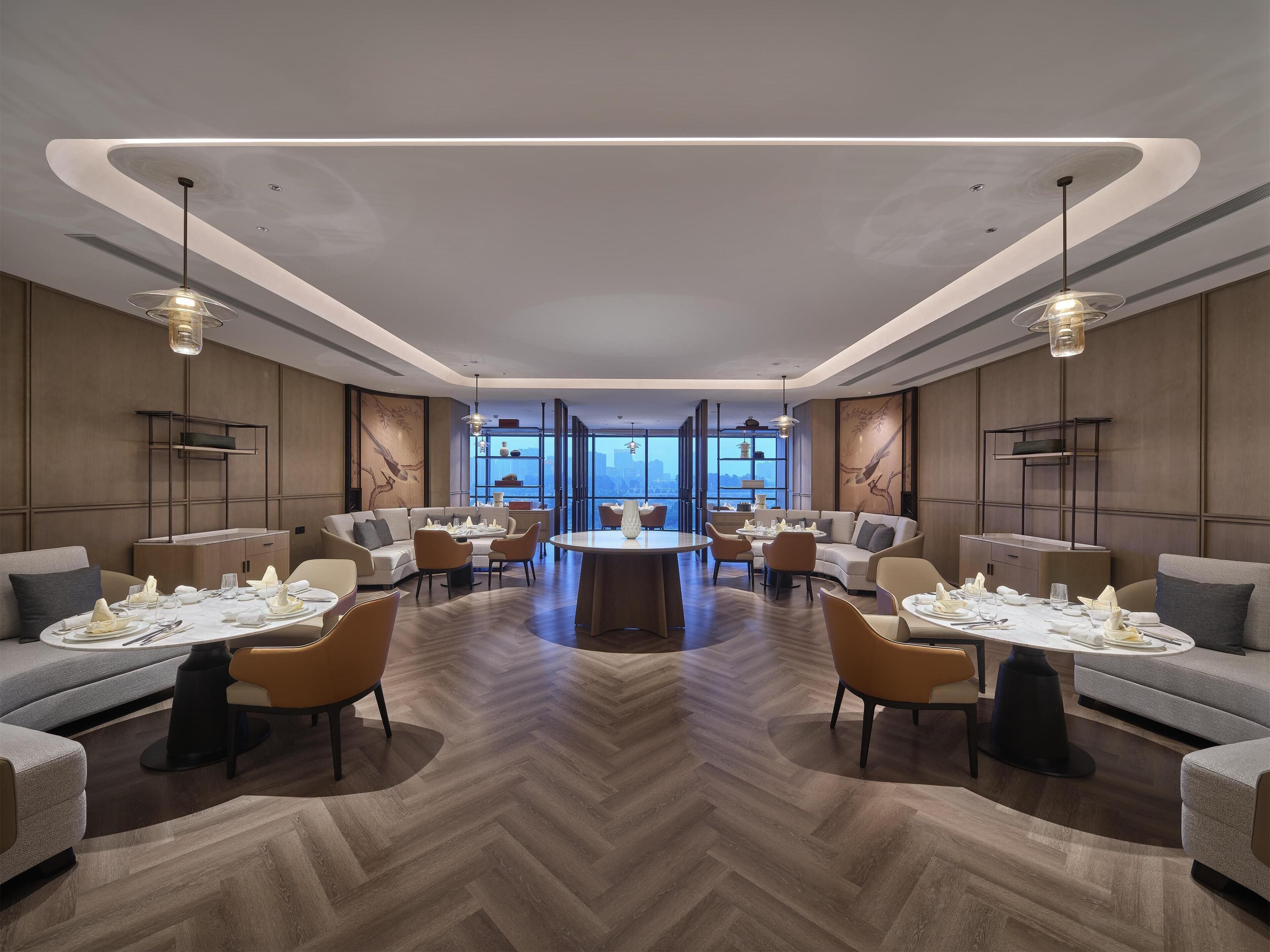 A modern hotel lobby with a central round table, sofas, and chairs arranged around it.