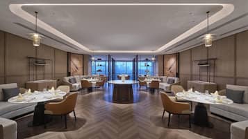 A modern hotel lobby with a central round table, sofas, and chairs arranged around it.