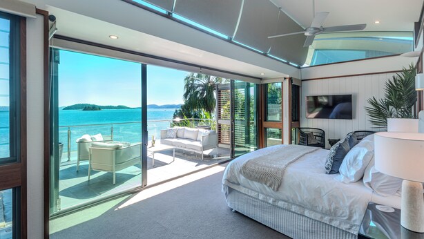 Een moderne slaapkamer met een groot bed, een televisie en een balkon met uitzicht op zee.