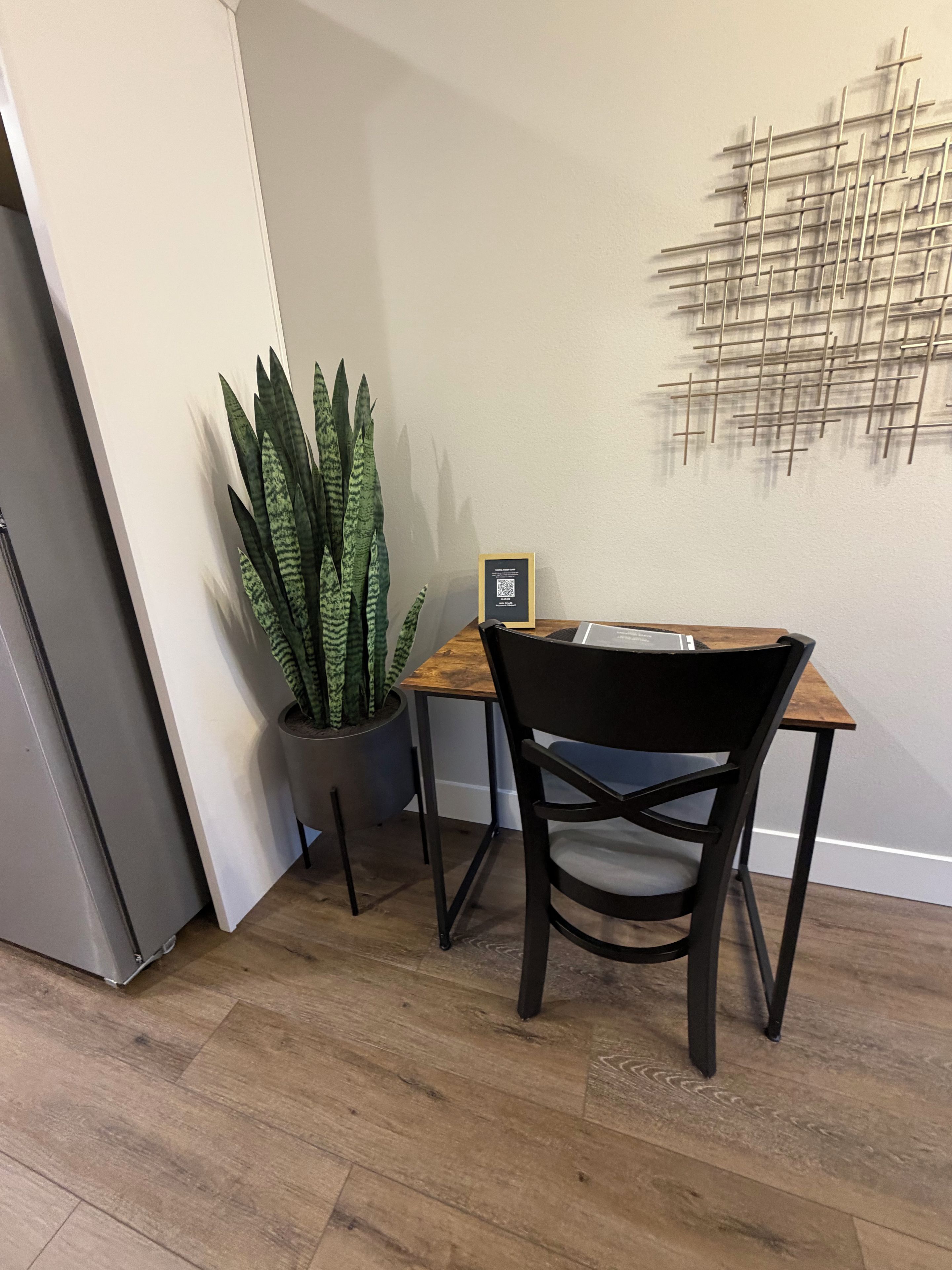 A dining area with a wooden table and a black chair, a potted plant, and a wall-mounted abstract art piece.
