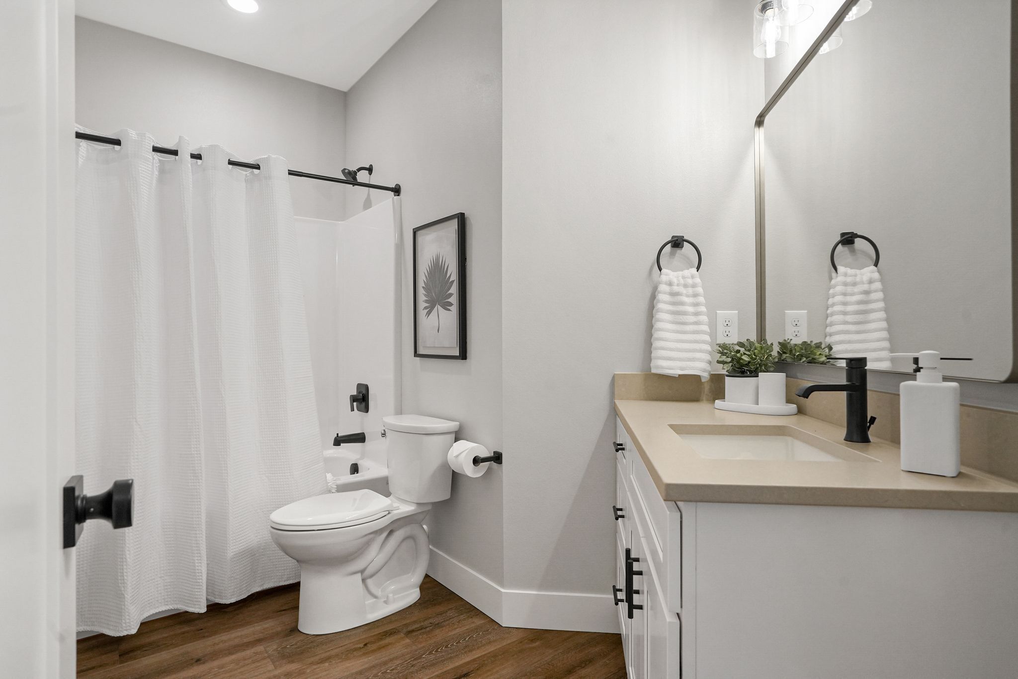 Ein modernes Badezimmer mit Toilette, Duschvorhang, Waschbecken, Spiegel und Handtuchhalter.