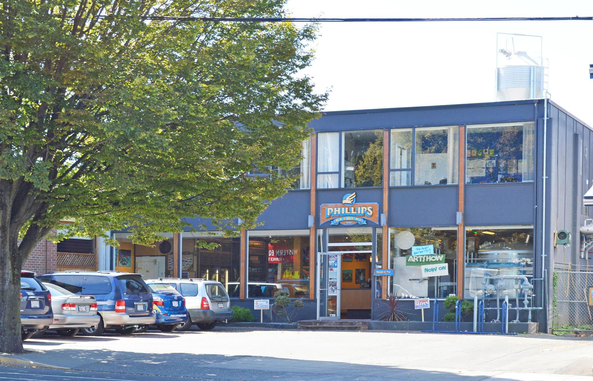 A building with a sign for 'Phillips Brewery' and a parking lot with several cars.