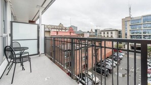 Un balcón con mesa y sillas, con vista a un estacionamiento y edificios.