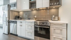Una cocina moderna con gabinetes blancos, microondas integrado, lavavajillas de acero inoxidable, horno doble y un lavadero.