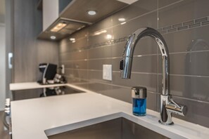 A modern kitchen with a stainless steel faucet, a white countertop, and a blue bottle on the sink. - Bright Old Town Suite with City Views (Victoria Central British Columbia Provincial Government)