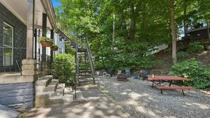 Un espace extérieur abrité, doté d’un escalier en pierre menant à un porche, une table de pique-nique et des jardinières suspendues.