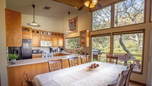 A spacious kitchen with wooden cabinets, a central island, and large windows offering a view of trees.