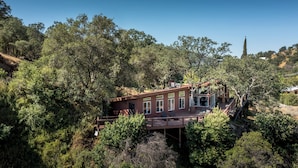 A modern house with a deck, surrounded by dense forest.
