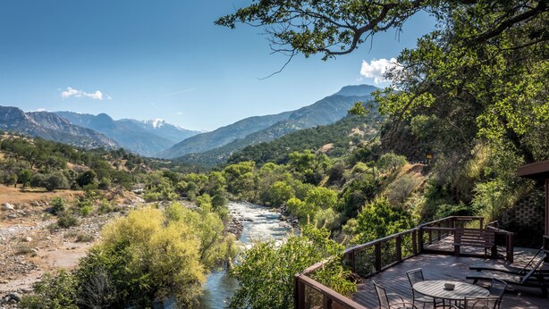 A deck with outdoor seating overlooking a river and mountains.