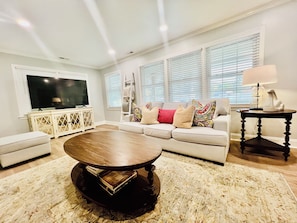 A living room with a large flat-screen TV, a sofa set, a coffee table, and a side table with a lamp. - Serenity Retread in Jacksonville NC  (Jacksonville)
