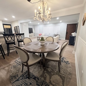 A dining area with a round table, chairs, a chandelier, and a kitchen in the background. - Serenity Retread in Jacksonville NC  (Jacksonville)
