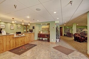 A reception area with a wooden desk, framed pictures on the walls, a large painting, and a seating area with leather chairs.