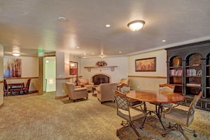 A spacious lounge area with a fireplace, comfortable seating, a dining table, and a bookshelf.