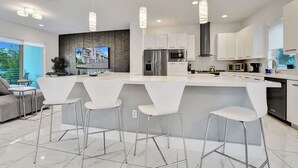 Een moderne keuken met een groot eiland, roestvrijstalen apparatuur en witte kasten.