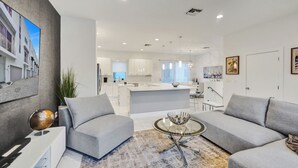 Een moderne woonkamer met een grijze bank, een glazen salontafel en een groot schilderij aan de muur.