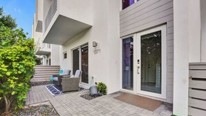 Een modern gebouw met een geplaveid terras, buitenmeubels en een deur met het nummer 1371.