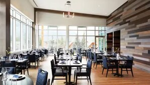 A spacious dining area with multiple tables and chairs, large windows offering a view of trees, and a modern wall design. - Mountain Getaway in Canmore! Sleeps 6 - Pool & Hottub (Canmore)