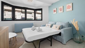 A room with a bed, a sofa, a small table, and a window with a view of buildings. - Studio Amanda - Welkeys (Nice)
