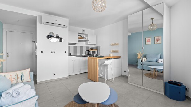 A modern, well-lit living room with a kitchen area, a dining table, and a sofa with towels. - Studio Amanda - Welkeys (Nice)