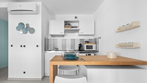 A modern kitchen with white cabinetry, a wooden dining table, and a built-in microwave. - Studio Amanda - Welkeys (Nice)
