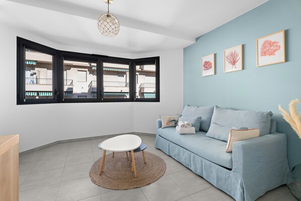 Une pièce avec un mur bleu clair, un canapé bleu, une table blanche aux pieds en bois, un tapis tissé et trois reproductions botaniques encadrées.