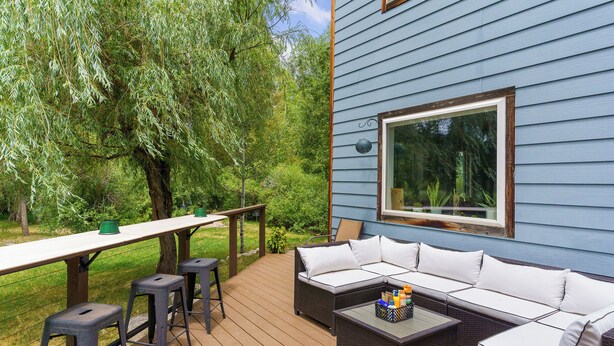 An outdoor deck with a sofa, bar stools, and a table. - Beautiful Home on River - 30 Day Rental Discounts! (Steamboat Springs)