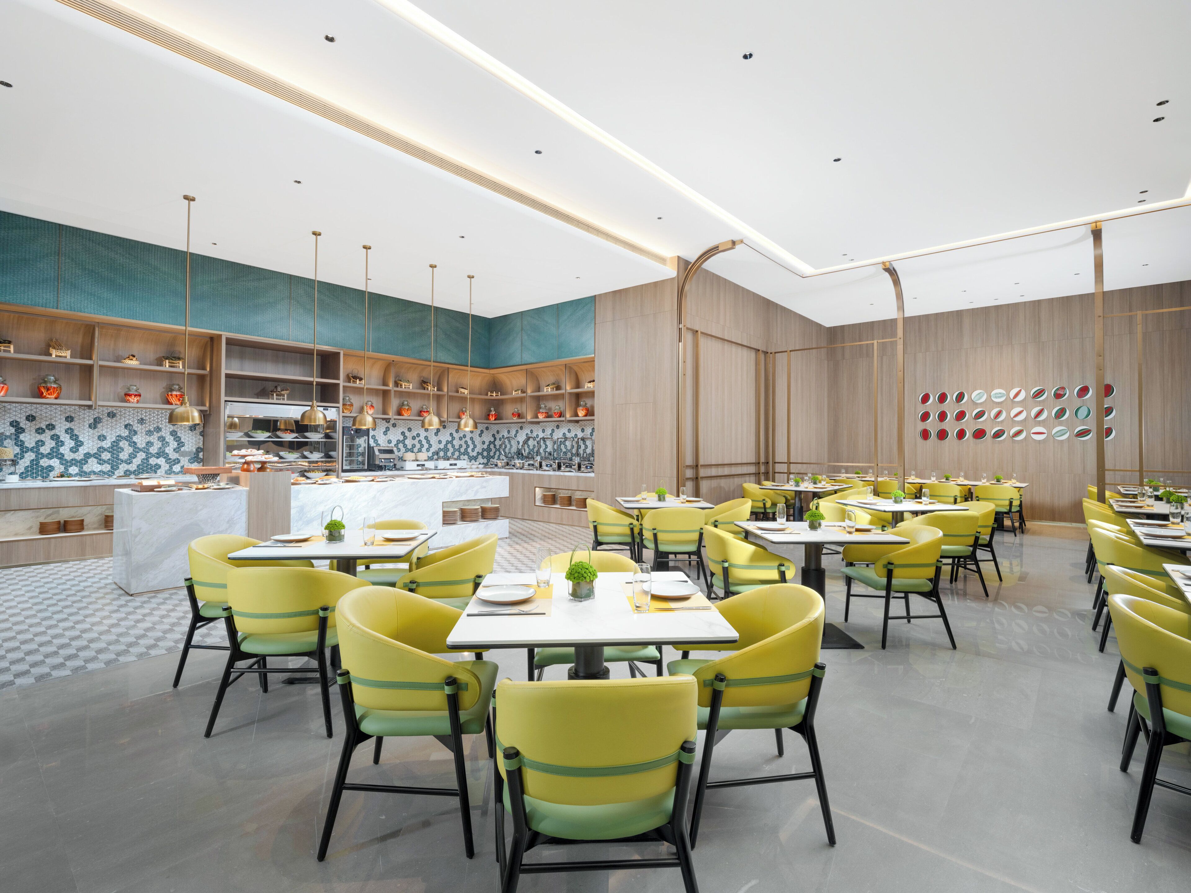 A modern restaurant with yellow chairs, a central island, and a patterned backsplash.