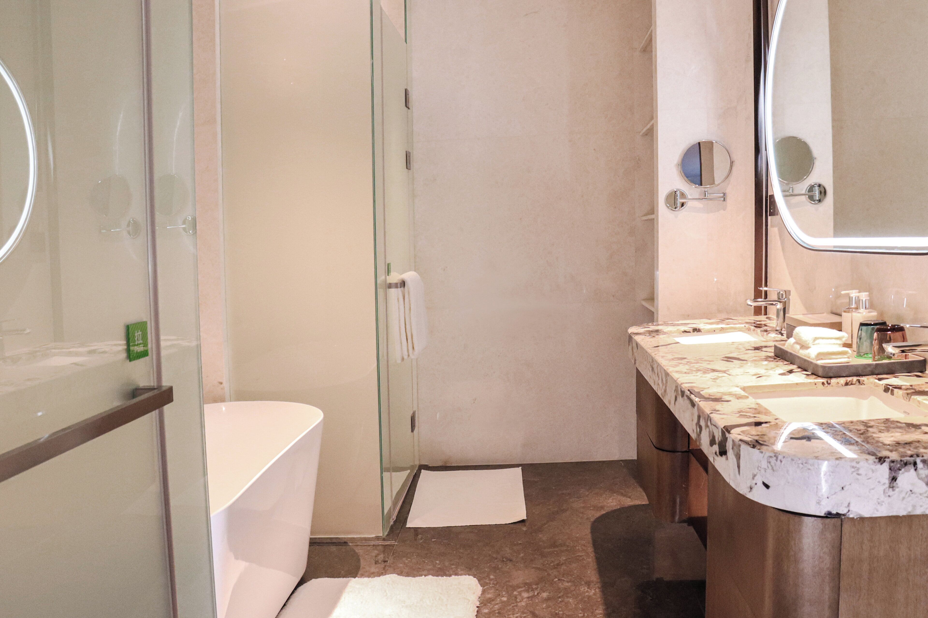 A bathroom with a glass shower enclosure, a white toilet, and a marble vanity with two sinks.