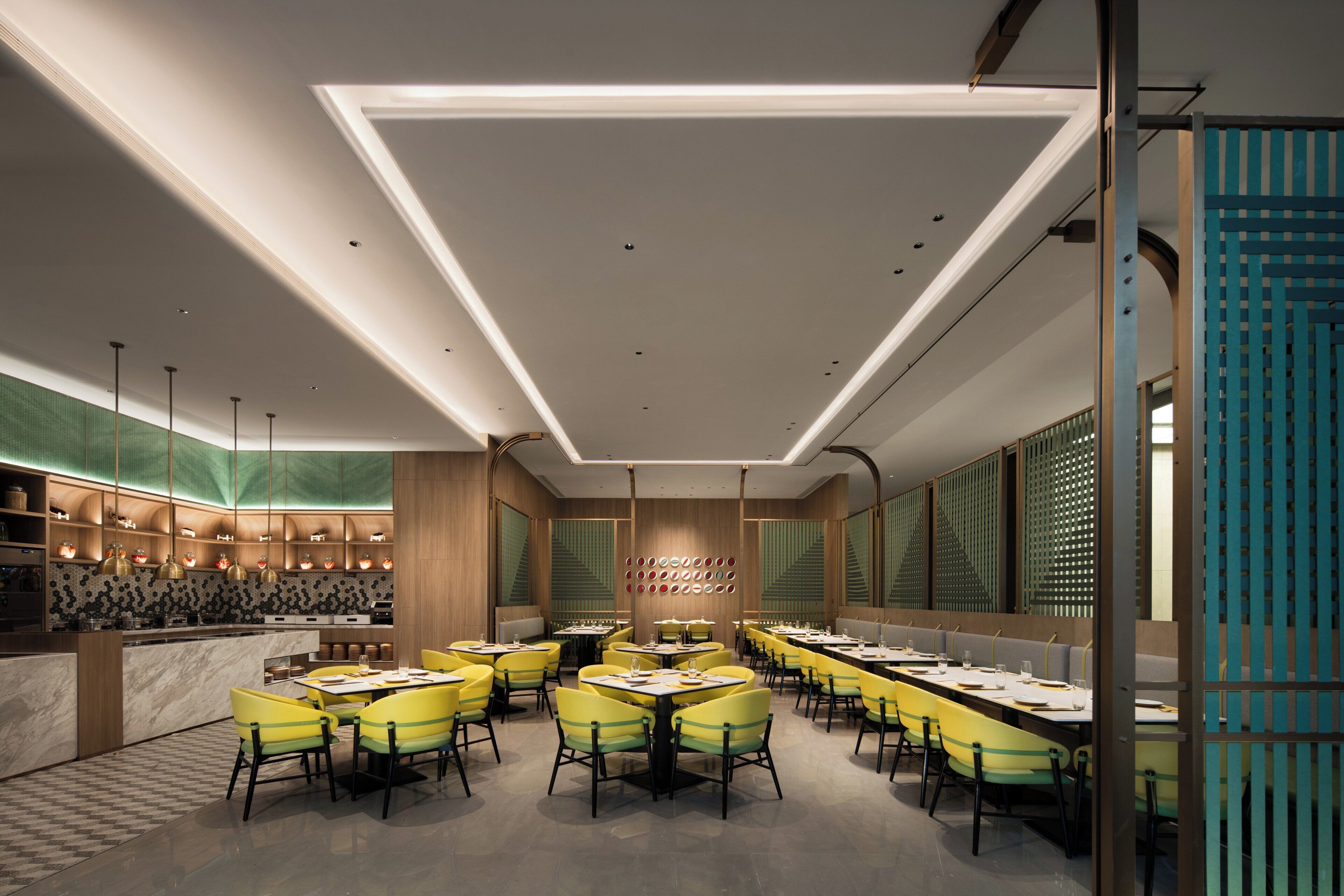 A modern dining area with multiple tables and chairs, a kitchen area, and a decorative wall with circular patterns.