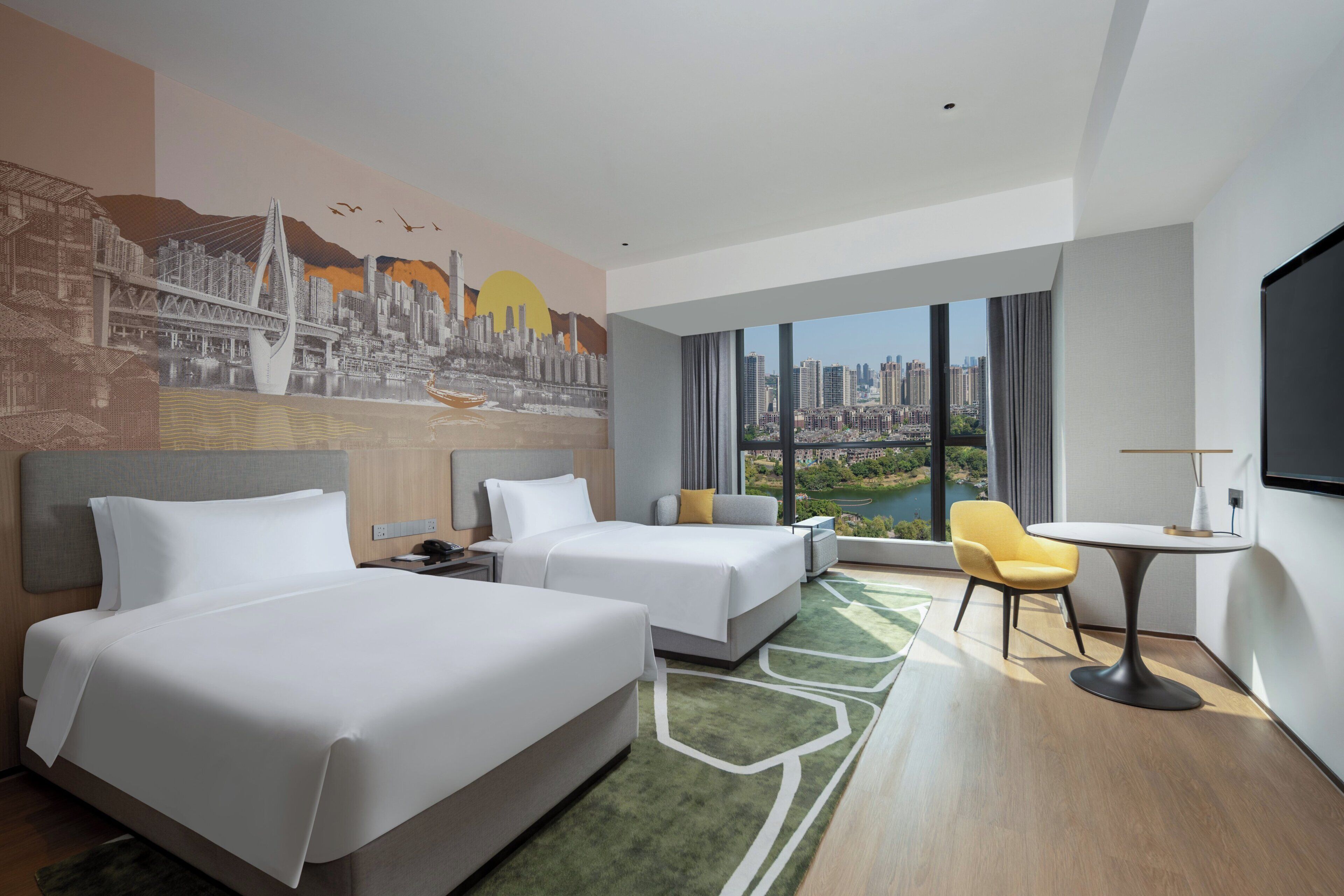 Habitación de hotel con dos camas, una mesa de comedor, una silla y un amplio ventanal con vista a la ciudad.
