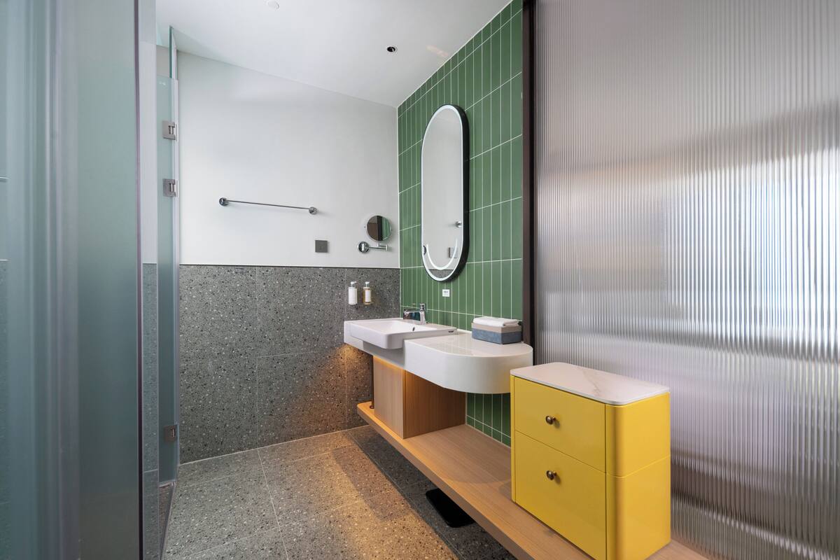 A modern bathroom with a glass shower enclosure, a vanity with two sinks, and a yellow cabinet.