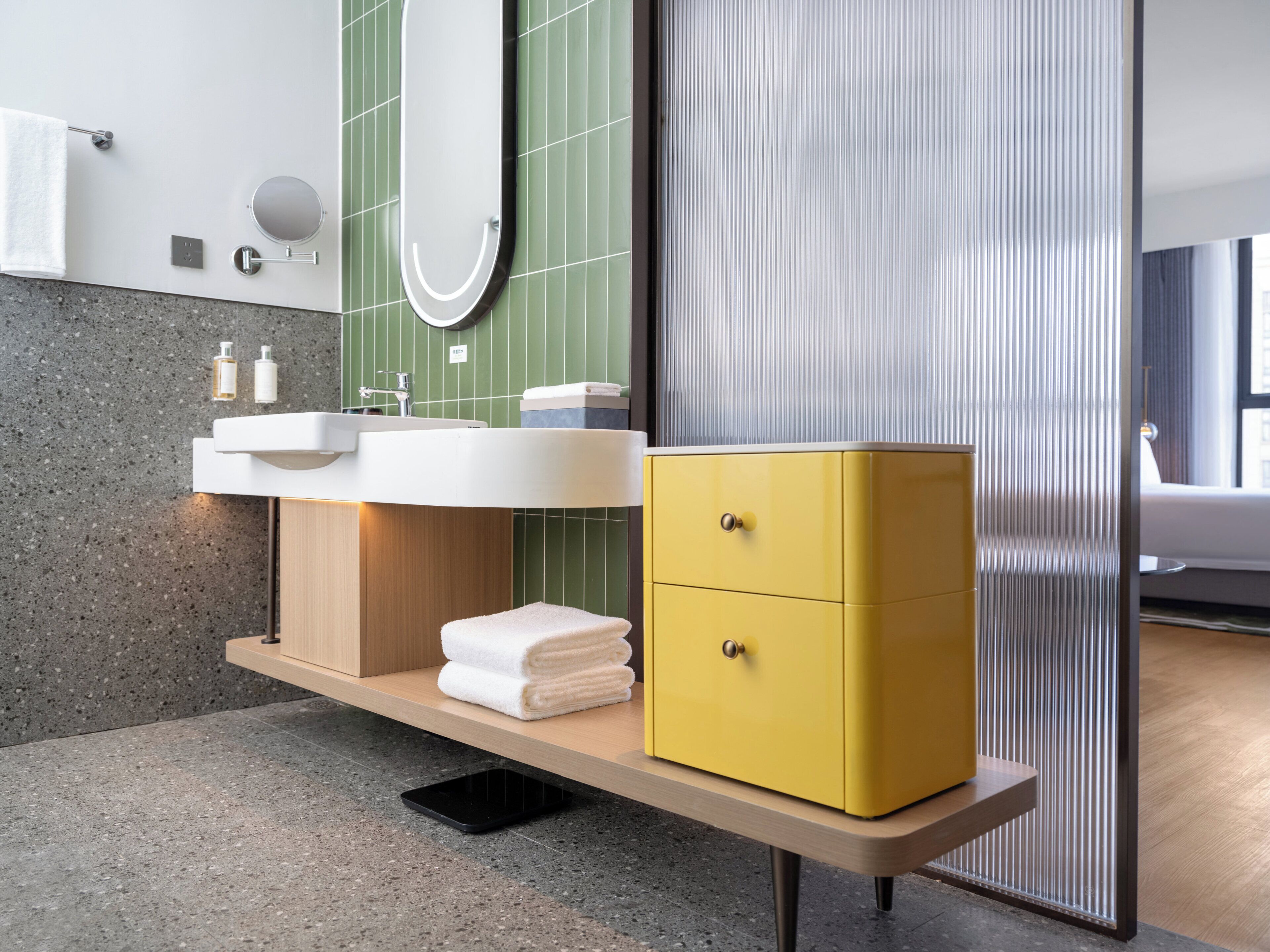 Ein modernes Badezimmer mit einem Holzlagerfläschchen, einem weißen Waschbecken, einem Spiegel und einem gelben Schrank.