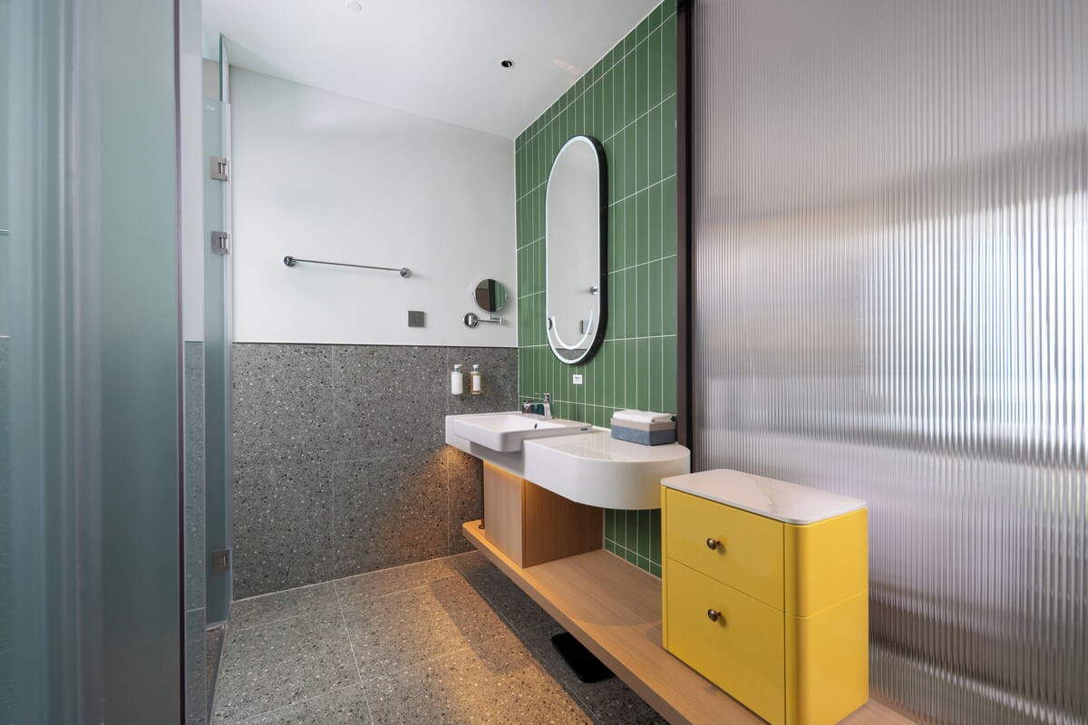 A modern bathroom with a glass shower enclosure, a vanity with two sinks, and a yellow cabinet.