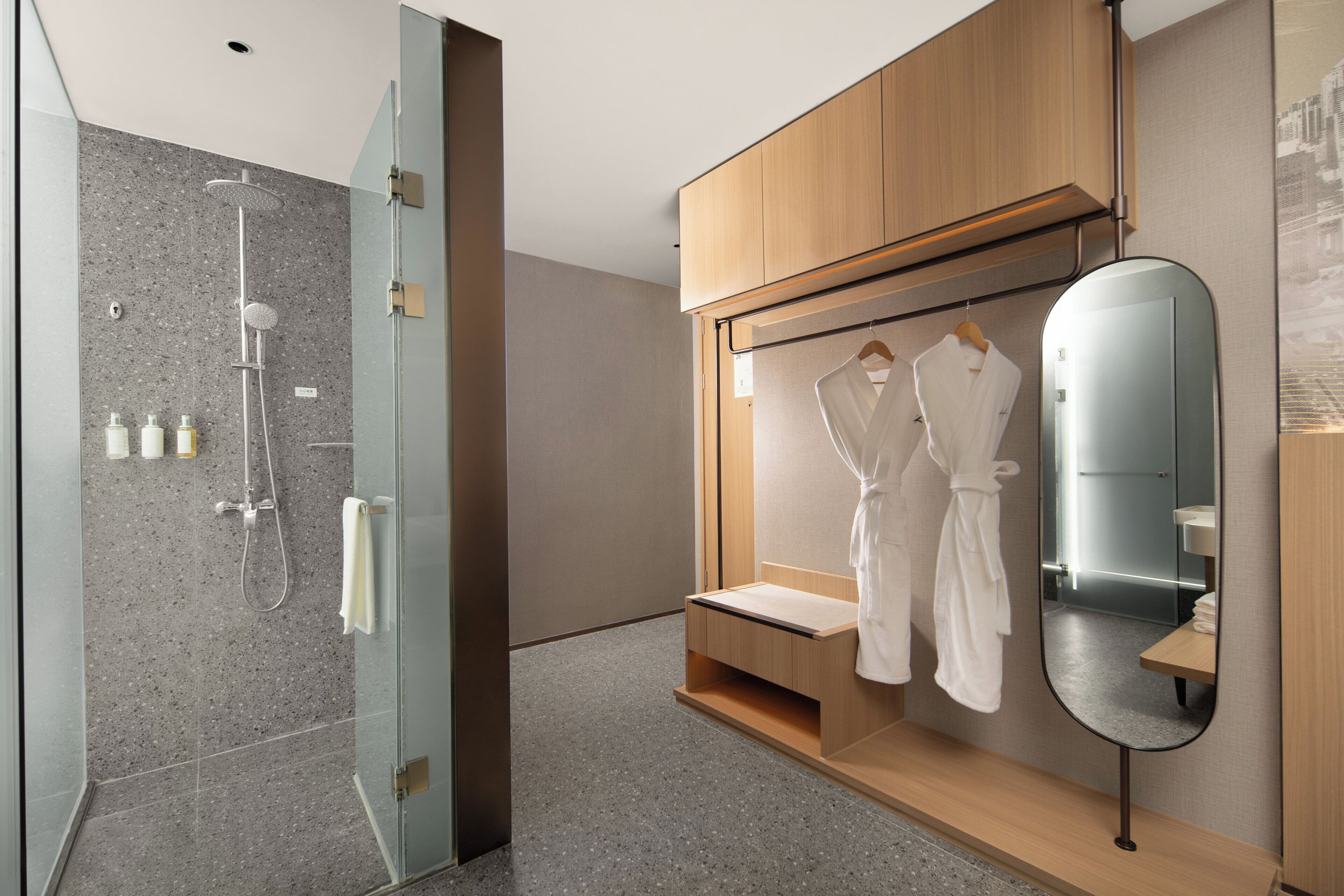 Un bagno moderno con cabina doccia in vetro, mobili contenitori in legno e uno specchio con piano di appoggio integrato.