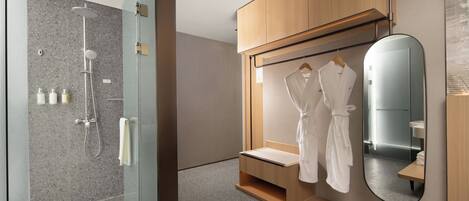 Un bagno moderno con cabina doccia in vetro, mobili contenitori in legno e uno specchio con piano di appoggio integrato.