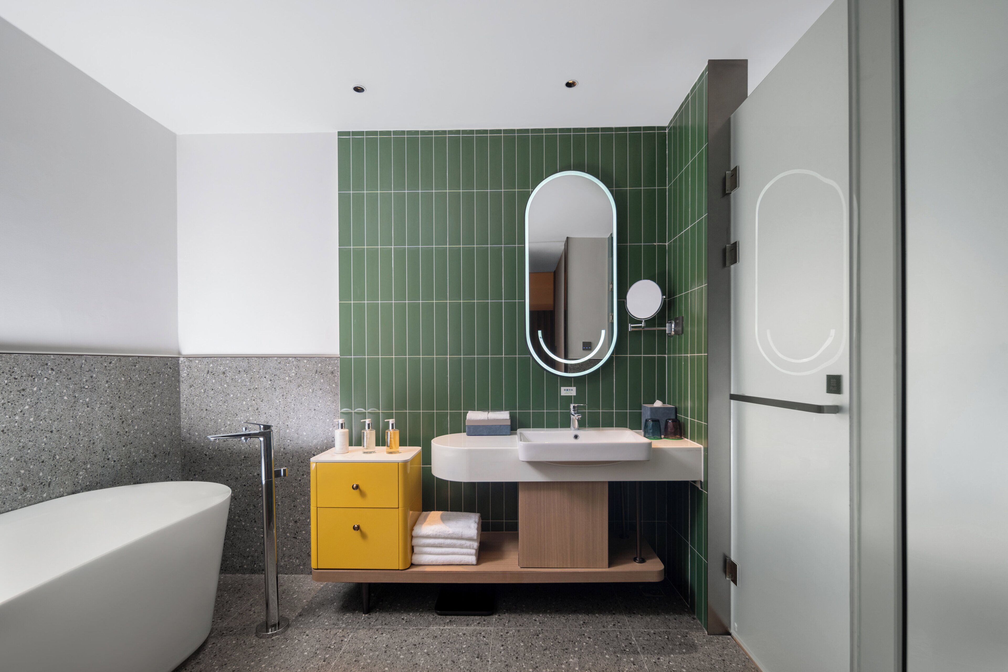 Un bagno moderno con una vasca freestanding, un mobile lavabo con specchio e pareti rivestite di piastrelle verdi.