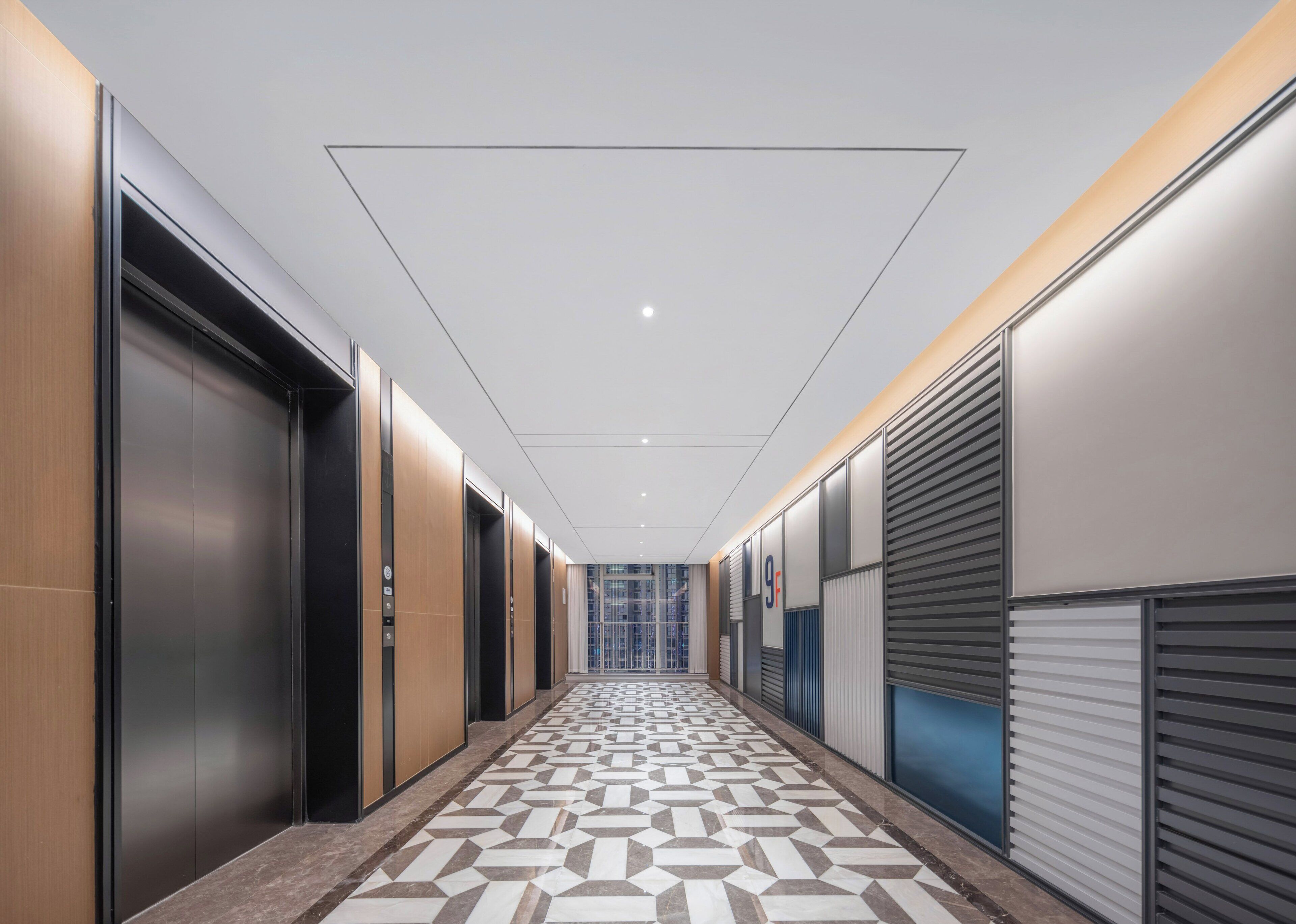 Un pasillo moderno con ascensores, suelo estampado y vistas del interior del edificio.