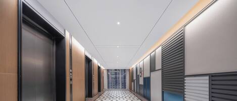Un pasillo moderno con ascensores, suelo estampado y vistas del interior del edificio.