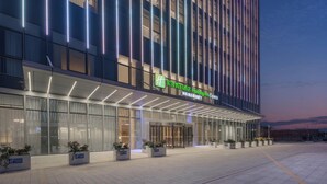 Un moderno edificio de hotel con un cartel llamativo de Holiday Inn Express, que cuenta con fachada de vidrio y un amplio recibidor con plantas en macetas.