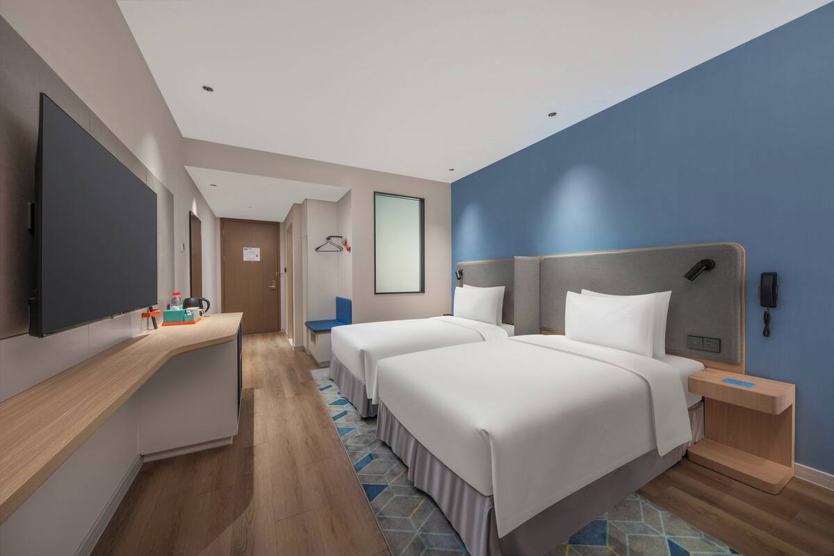 A hotel room with two beds, a desk, a flat-screen TV, a bedside table, and a wall-mounted phone.