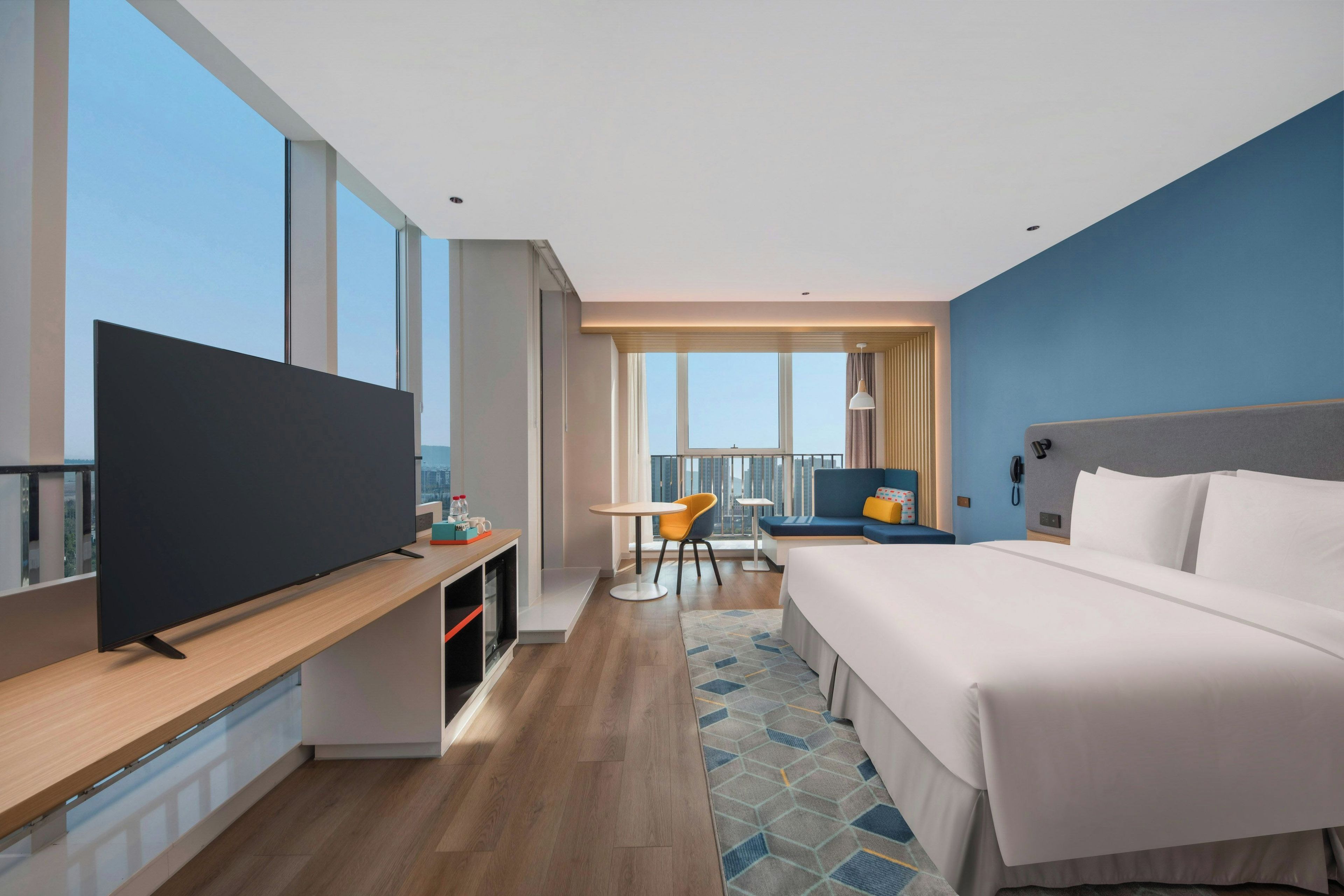 Habitación de hotel moderna con una cama grande, televisión, escritorio y balcón con vista a la ciudad.