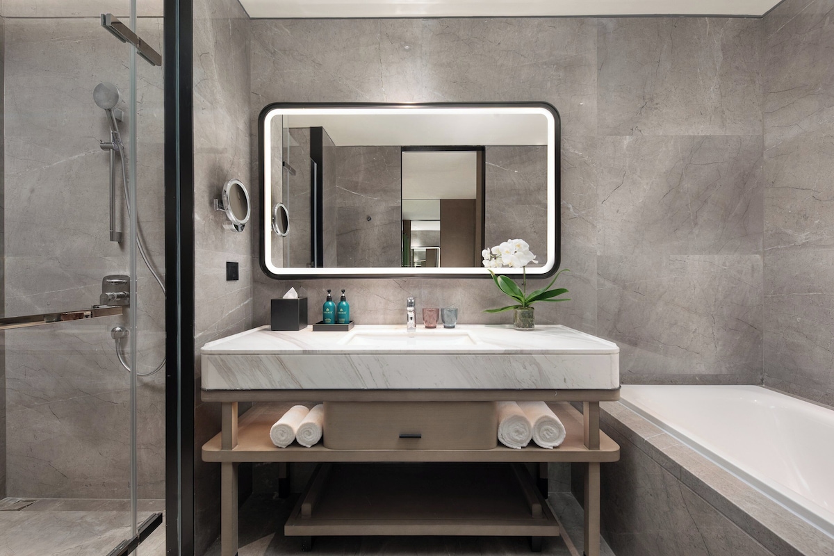 A modern bathroom with a large mirror, a bathtub, and a shower area.
