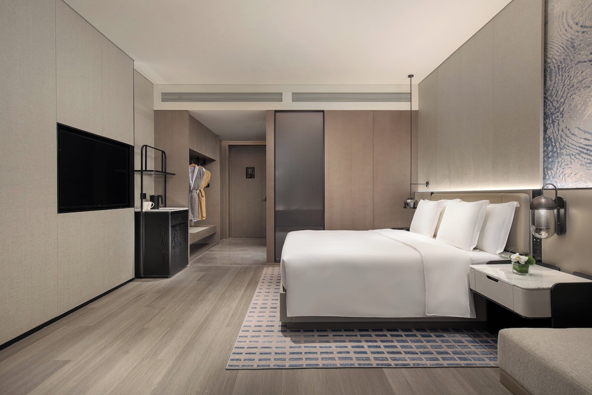 A modern hotel room with a large bed, bedside table, and a flat-screen TV mounted on the wall.