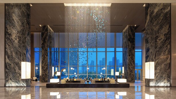 A spacious lobby with marble walls, a central reception desk, and large windows offering a city view. - Crowne Plaza Jingmen by IHG (Jingmen)