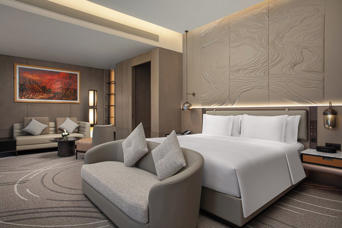 Ein modernes Hotelzimmer mit einem großen Bett, einer Couch, einem Couchtisch und einem Gemälde an der Wand.