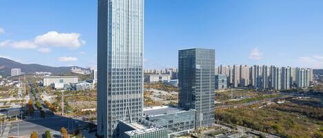 A modern high-rise building complex with a glass facade, surrounded by a well-maintained park and a road.