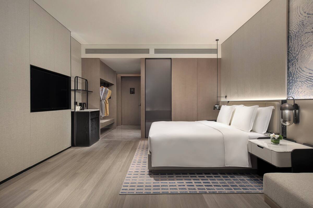 A modern hotel room with a large bed, bedside table, and a flat-screen TV mounted on the wall.